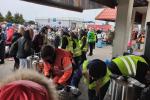 Przejście graniczne na zewnątrz - na pierwszym planie wolontariusze w żółtych kamizelkach oraz ratownik medyczny, którzy stoją przy garnkach i termosach i przygotowują jedzenie. W tle wolontariusze, którzy rozdają jedzenie oraz dużo obywateli Ukrainy.