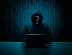 Postać hakera siedzącego w mroku, ma kaptur na głowie i nie widać mu twarzy, przed nim stoi laptop