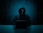 Na ciemnym zdjęciu widać w mroku sylwetkę hakera w czarnej bluzie, ma nałożony kaptur i nie widać jego twarzy, przed im stoi laptop.